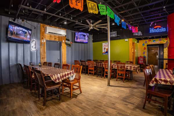 Colorful private dining space in a Mexican restaurant featuring papel picado, wood-paneled walls, TVs, and festive lighting — ideal for parties, events, or game day gatherings.