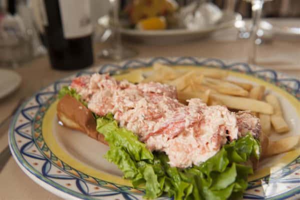 Lobster roll on white plate next to fries