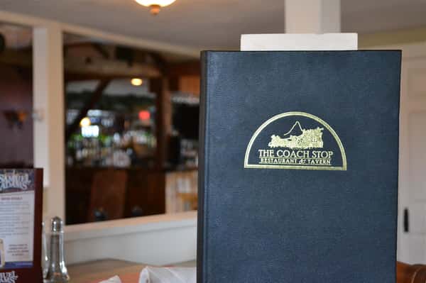 Blue menu book with lable The coach Stop Restaurant & tavern on table