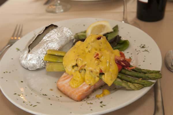 Salmon covered with vegetables and yellow sauce next to baked potato