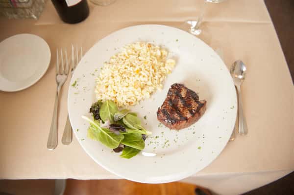 Char Grilled steak with rice pilaf and greens on a white plate