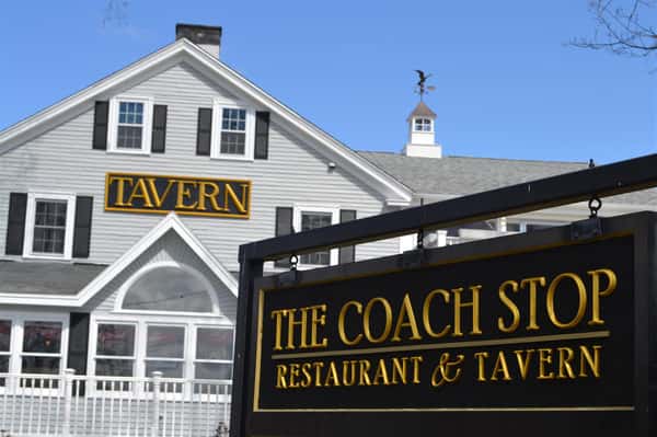 Exterior of White paneled building with "Tavern" sign in middle next to sign saying "The Coach Stop Restuarant & Tavern"