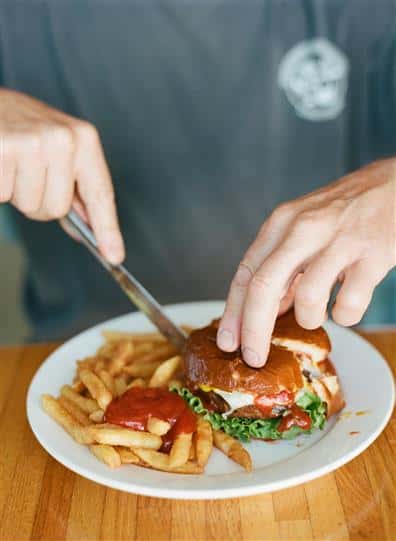 man cutting into a cheeseburger with a side of a fries