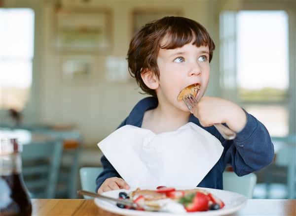 young child eating a plate of pancakes with fresh fruit