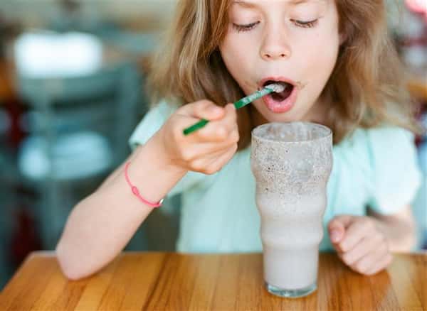 young child smiling at the camera holding eating a shake