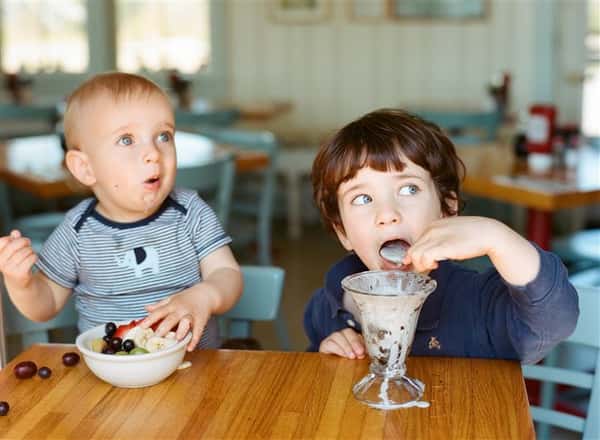 two young children eating food and desserts