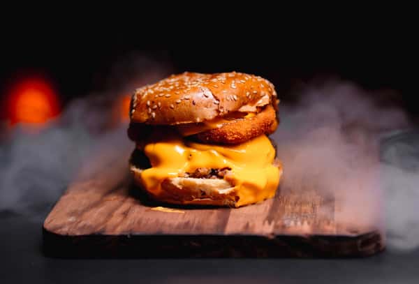 Mouthwatering cheeseburger with melted cheese and steam rising against dark background.