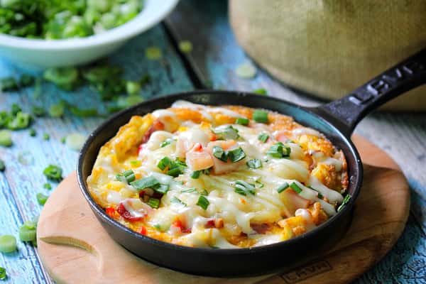 Cheesy loaded potato skillet topped with bacon, green onions, and melted cheese served hot in a cast iron pan.