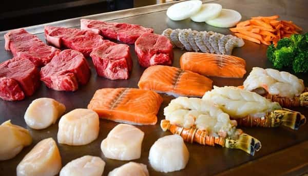 hibachi stovetop with raw chicken, lobster, salmon, beef, and vegetables