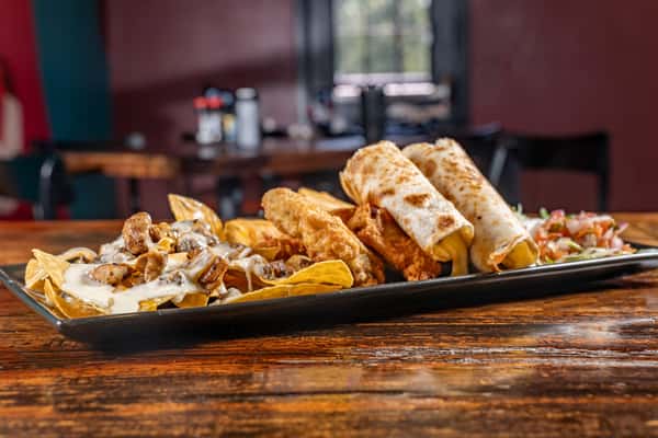 Assorted Mexican appetizers featuring cheesy nachos, crispy chicken tenders, flautas, and fresh pico de gallo on a rectangular black plate.