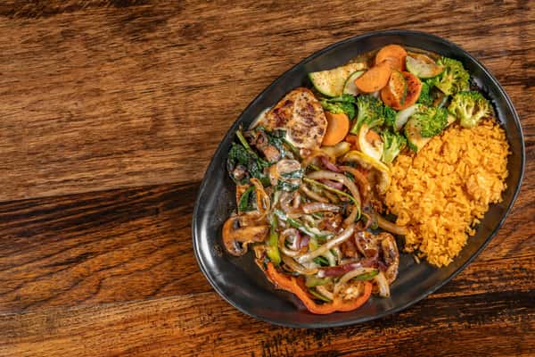 Grilled chicken breast topped with sautéed onions and peppers, served alongside Mexican rice and seasoned mixed vegetables on a black plate.