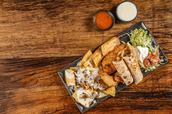 Assorted Mexican appetizers including cheesy nachos, taquitos, quesadillas, fried chicken tenders, guacamole, sour cream, and pico de gallo, served with salsa and queso dips.