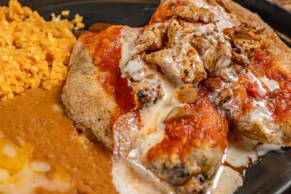 Two stuffed chile rellenos topped with grilled chicken, red sauce, and melted cheese, served with refried beans and Mexican rice for a hearty Tex-Mex entrée.