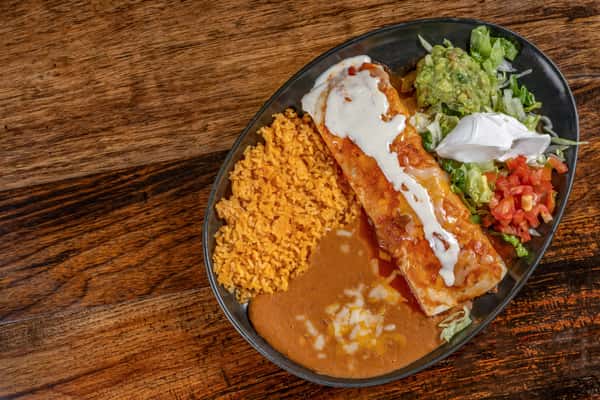 Cheese-smothered enchilada with Mexican rice, refried beans, shredded lettuce, guacamole, sour cream, and pico de gallo on a black oval plate.