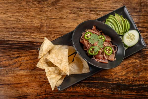 Fresh ahi tuna ceviche topped with sliced jalapeños and cilantro, served with crispy tortilla chips, avocado slices, and cucumber on a sleek black plate.