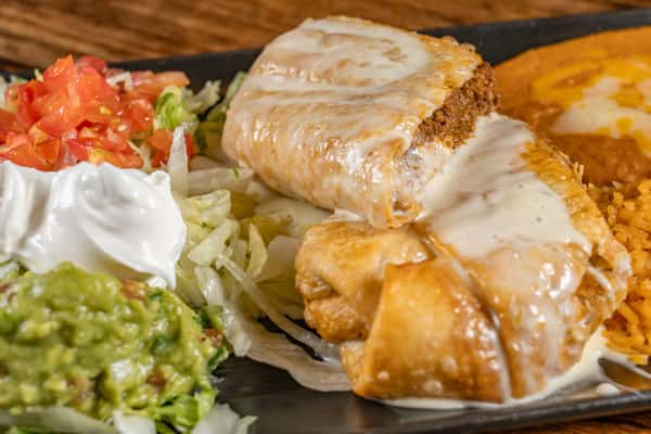 Beef chimichanga topped with creamy queso, paired with Mexican rice, refried beans, guacamole, sour cream, shredded lettuce, and fresh pico de gallo.