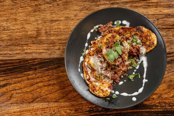 Grilled poblano peppers stuffed and topped with seasoned chorizo and creamy white sauce, garnished with fresh cilantro on a black plate over rustic wood.