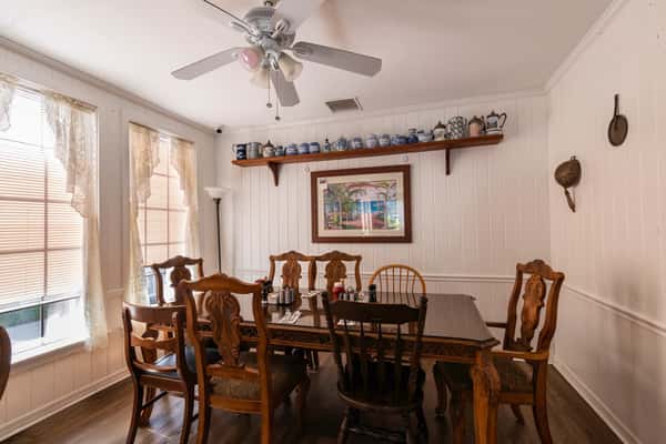 Charming private dining room featuring antique chairs, a ceiling fan, white-paneled walls, and a shelf lined with decorative teapots — a quaint and cozy setting for small group meals.