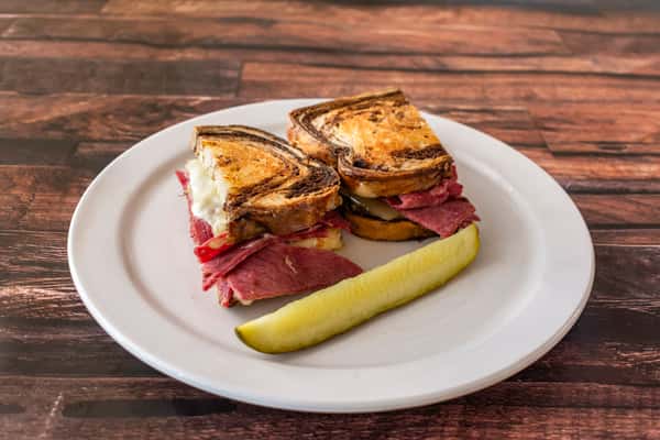 Top view of a stacked Reuben sandwich with layers of corned beef and Swiss cheese on marbled rye, served with a dill pickle spear — a hearty and flavorful deli lunch.
