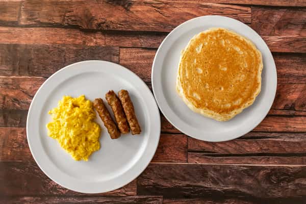 Fluffy scrambled eggs and sausage links on one plate, paired with a stack of golden pancakes on a separate plate — a classic American breakfast combo served on clean white dishes.