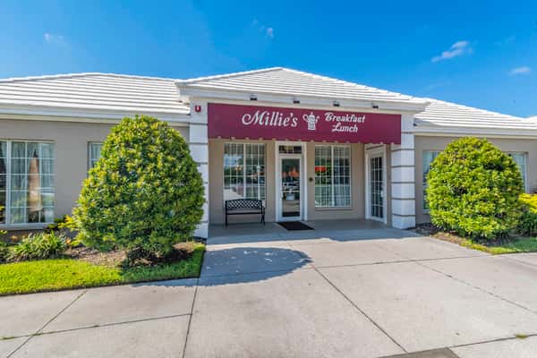 Daytime exterior view of Millie's Breakfast & Lunch with manicured shrubs, a maroon awning, and white-trimmed windows — a welcoming spot for homestyle morning and midday meals.