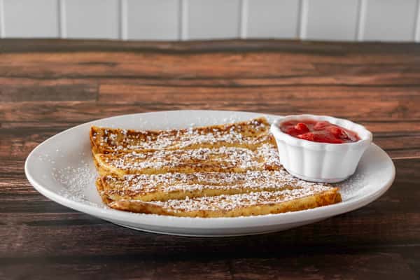 Side view of sliced French toast sticks topped with powdered sugar and paired with a ramekin of strawberry topping — a comforting breakfast option with sweet appeal.