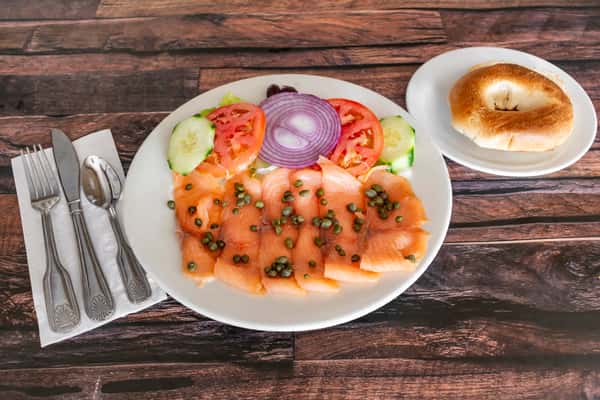 Smoked salmon lox plate with capers, sliced tomatoes, red onions, and cucumbers, served alongside a toasted bagel — a classic New York–style brunch dish.