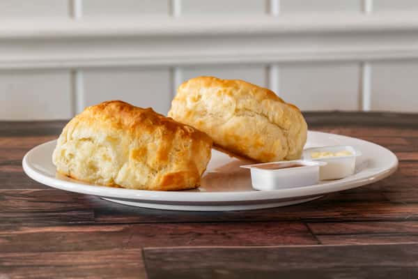 Flaky homemade biscuits served with butter and jelly cups on the side — a warm and simple Southern-style breakfast staple.