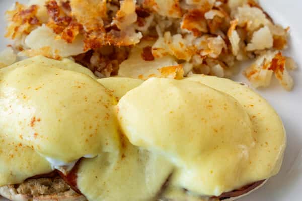 Close-up of classic eggs Benedict smothered in rich hollandaise sauce, served with crispy golden home fries — a savory brunch staple for breakfast lovers.