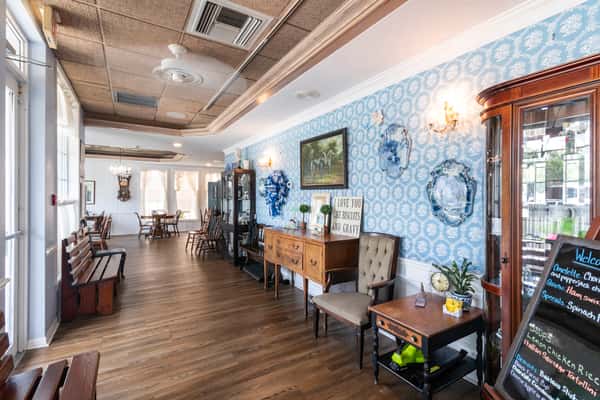 Charming restaurant entrance with blue patterned wallpaper, vintage furnishings, decorative plates, and warm wood flooring — a welcoming and homey ambiance for breakfast or lunch diners.
