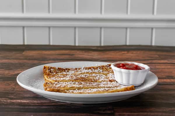 Side view of golden French toast sticks dusted with powdered sugar, served with a small ramekin of strawberry topping — a kid-friendly breakfast treat in a charming, casual dining setting.