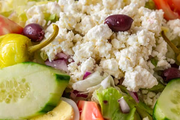 Close-up of a Greek salad featuring crumbled feta cheese, Kalamata olives, cucumbers, tomatoes, red onion, and pepperoncini over crisp romaine lettuce — a colorful and zesty Mediterranean favorite
