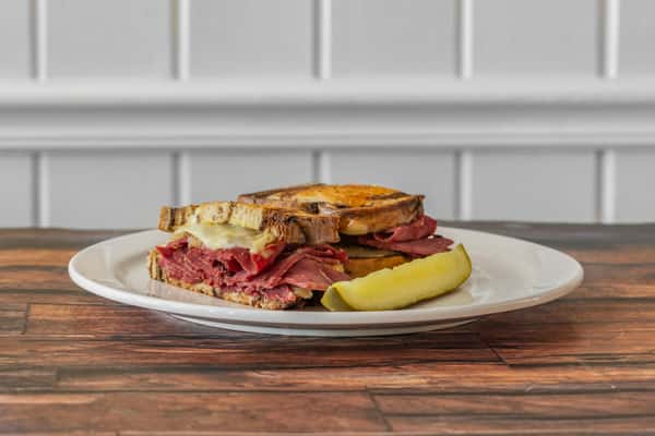 Hot Reuben sandwich stacked with sliced corned beef, melted Swiss cheese, and rye bread, served with a crisp dill pickle spear — a savory deli-style lunch classic.