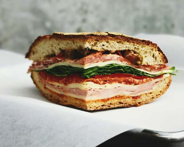 Thick deli sandwich layered with turkey, salami, cheese, spinach, and pickled vegetables on rustic multigrain bread.