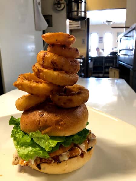 Burger with lettuce, sauce, with a skewer going through the top holding stack of onion rings