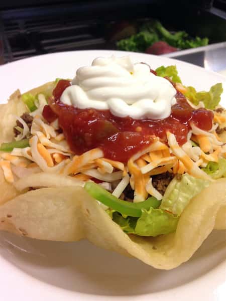 Taco bowl with tortilla shell with meat, lettuce, cheese, sour cream, and salsa