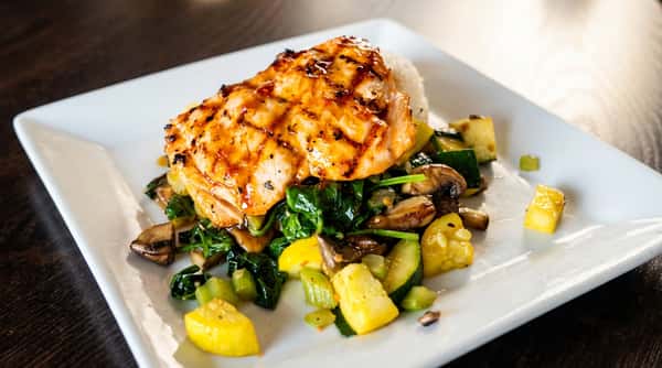 Grilled salmon with rice, spinach, zucchini, mushrooms, and yellow squash on a white plate.