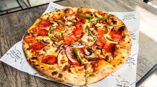 Pizza with pepperoni, sausage, green bell peppers, red onion, mushrooms, and cherry tomatoes on a white paper.