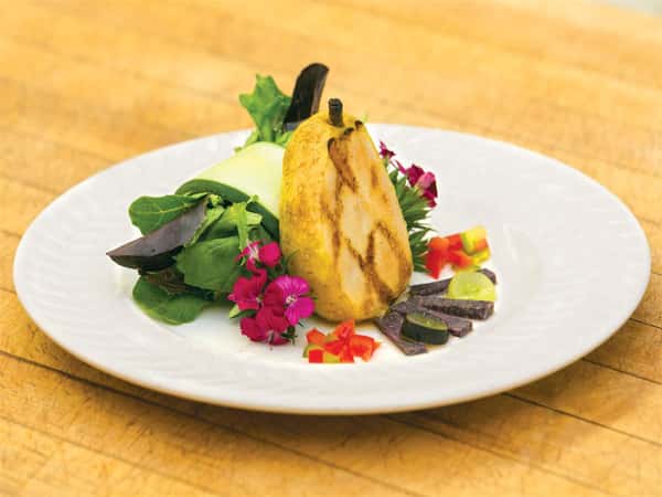 grilled pear dessert on a plate with edible flowers