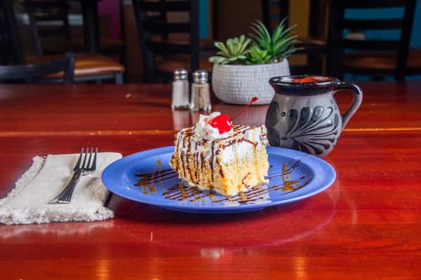 Slice of tres leches cake topped with whipped cream and a cherry