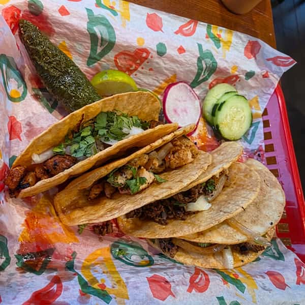 Authentic street tacos filled with grilled chicken and seasoned steak, topped with fresh cilantro and onions, served with grilled jalapeño, lime, radishes, and cucumber at El Cazo Mexican Restaurant.