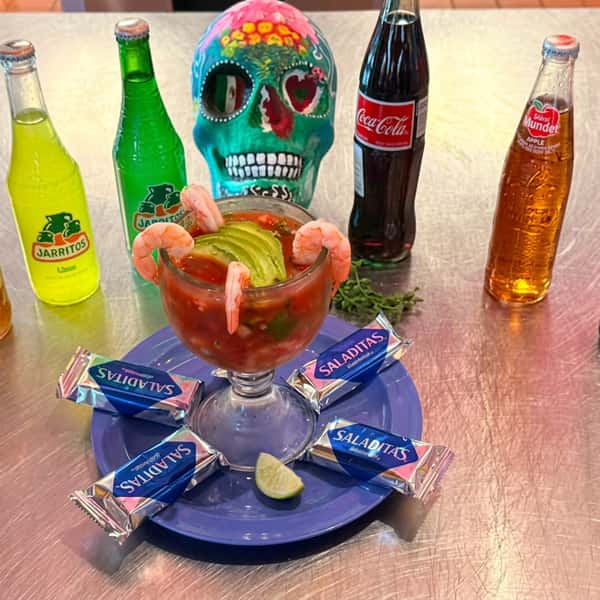 Mexican shrimp cocktail garnished with fresh avocado, shrimp, and lime, served with traditional crackers and assorted Mexican sodas at El Cazo Mexican Restaurant.