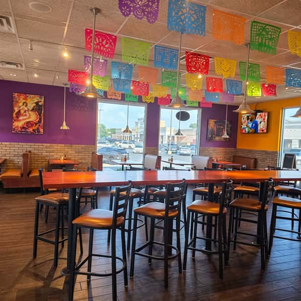 Spacious dining room at El Cazo Mexican Restaurant featuring colorful papel picado decorations, comfortable booths, communal seating, and a warm, family-friendly atmosphere.