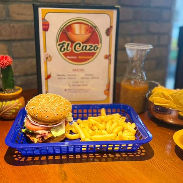 Burger and crispy French fries served at El Cazo Mexican Restaurant with fresh tortilla chips, house salsa, and the restaurant menu displayed in a warm, casual dining setting.