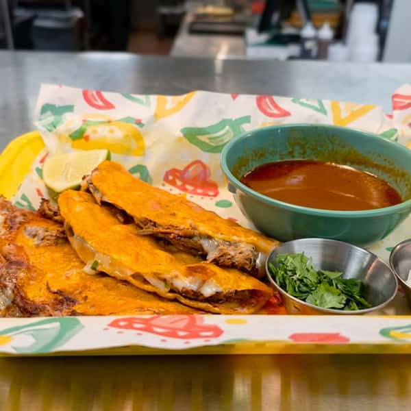 Birria quesatacos filled with slow-cooked beef and melted cheese, served with rich consommé, fresh cilantro, and lime at El Cazo Mexican Restaurant.