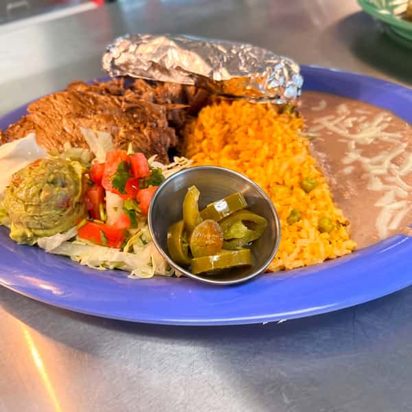 Grilled carne asada served with Mexican rice, refried beans topped with melted cheese, a baked potato, fresh guacamole, pico de gallo, jalapeños, and salad at El Cazo Mexican Restaurant.