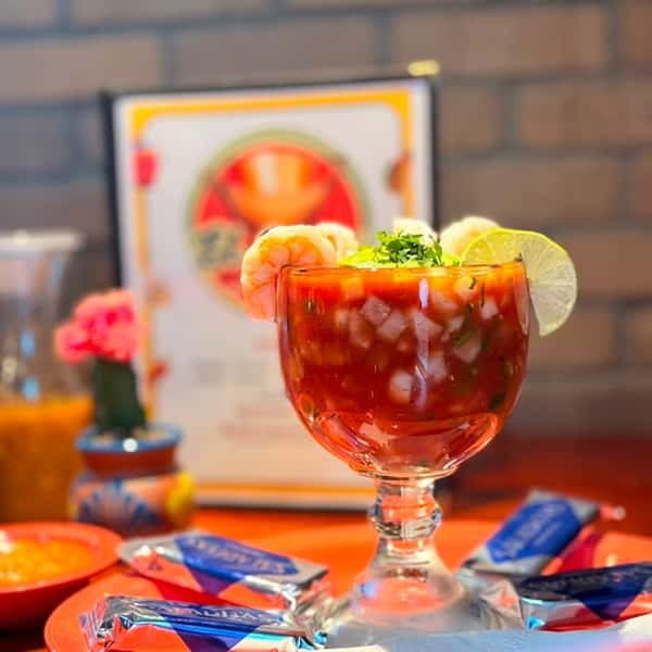 Fresh Mexican shrimp cocktail served with shrimp, tomato, onion, cilantro, and lime in a chilled goblet at El Cazo Mexican Restaurant.