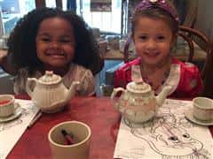 Two children sitting at table with teapots and coloring pages