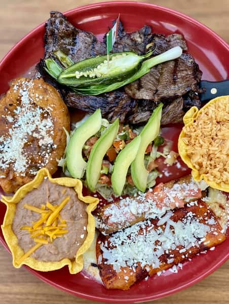 Mexican combination platter with carne asada, chile relleno, enchiladas, refried beans, rice, avocado, and pico de gallo.