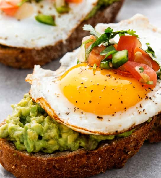 Avocado toast with a fried egg, pico de gallo, and cilantro on toasted brown bread.